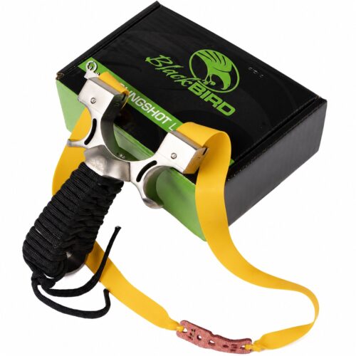 Metal Y-shaped slingshot with yellow elastic bands and a black, cord-wrapped handle, resting on a black box with green branding (BlackBird).